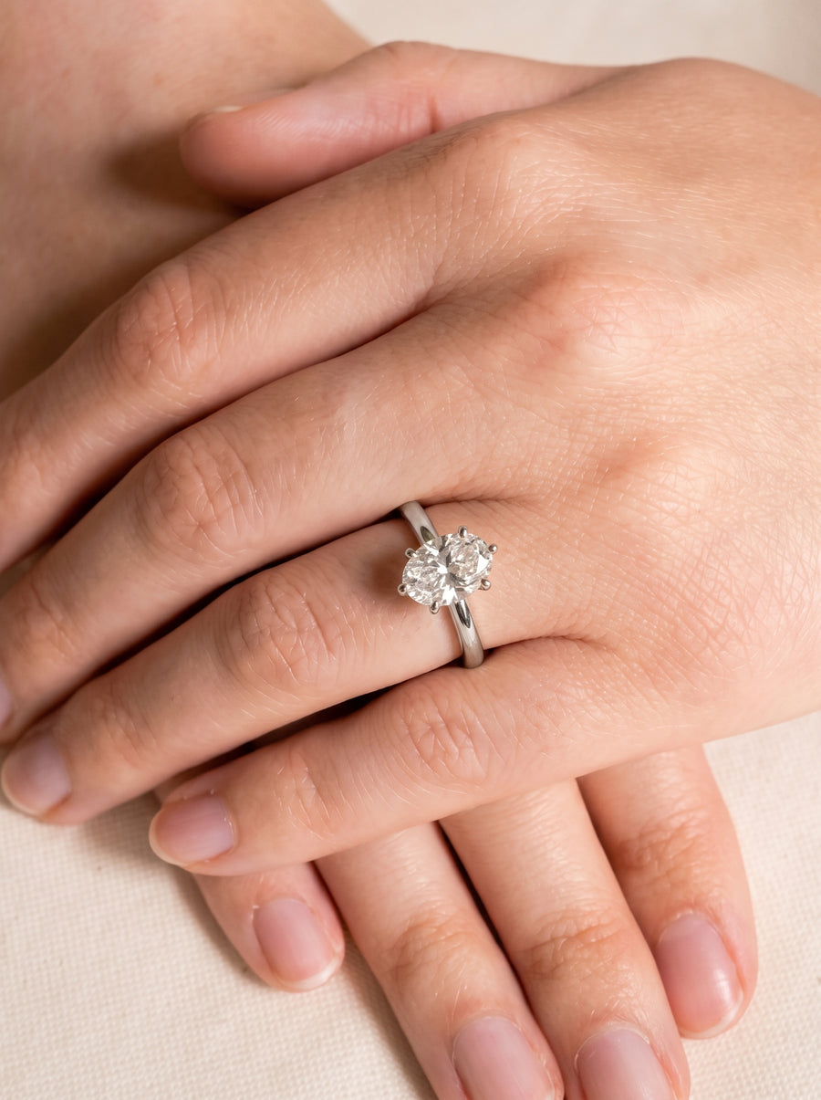 Oval diamond engagement ring with a twisted silver band worn on a finger.