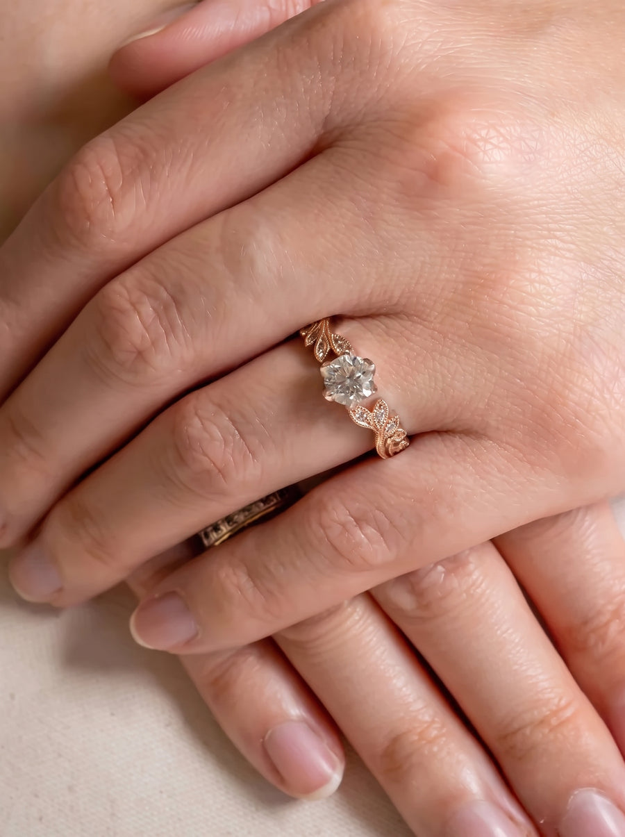 Rose gold engagement ring with a round diamond and leaf-shaped band on a finger.