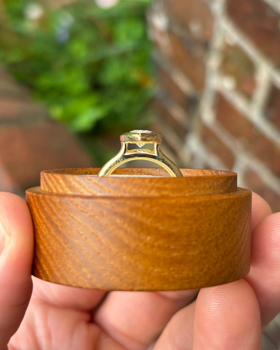 Marquise cut lab-grown diamond engagement ring in a gold bezel cathedral setting held in a wooden box.