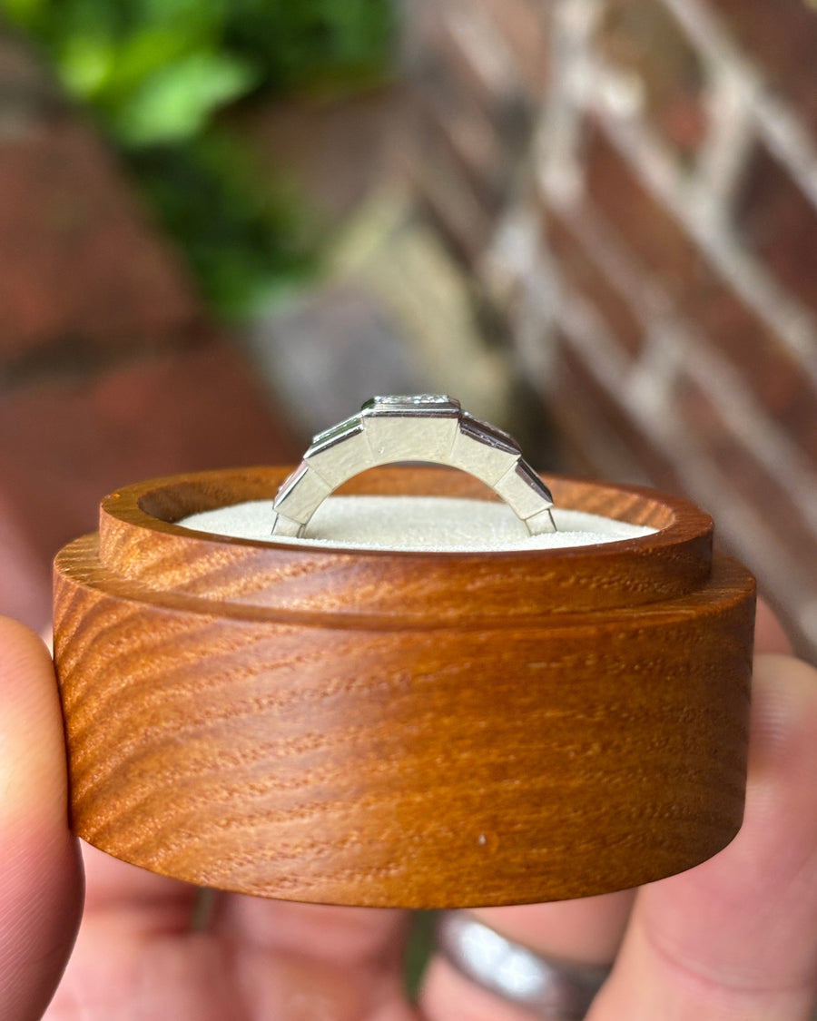 Five-stone princess cut diamond ring in a silver-toned metal setting, displayed in a round wooden box.