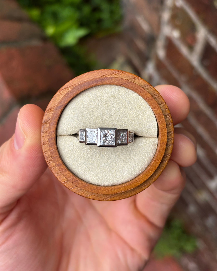 Five-stone princess cut diamond ring in a platinum setting held in a round wooden box.