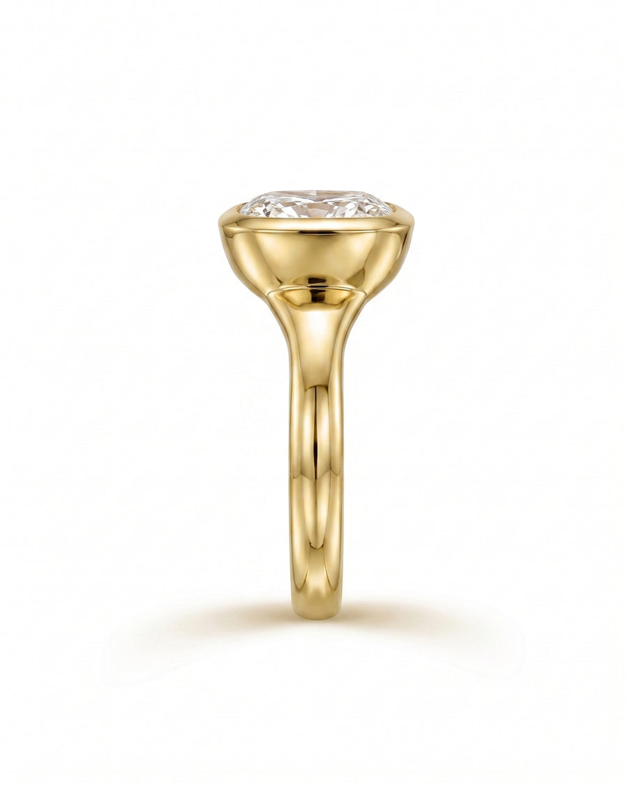 Gold engagement ring with a chunky cushion cut diamond in a bezel setting.
