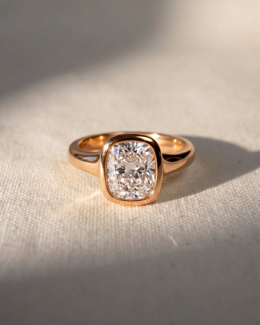 Rose gold engagement ring with a chunky cushion cut diamond in a bezel setting.