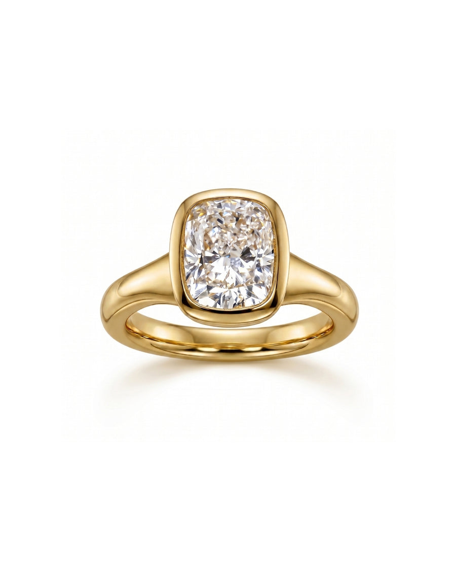 Gold engagement ring with a chunky cushion cut diamond in a bezel setting.