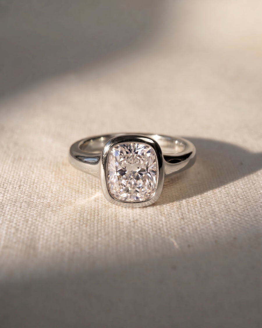 Silver ring with a chunky cushion cut diamond in a bezel setting.