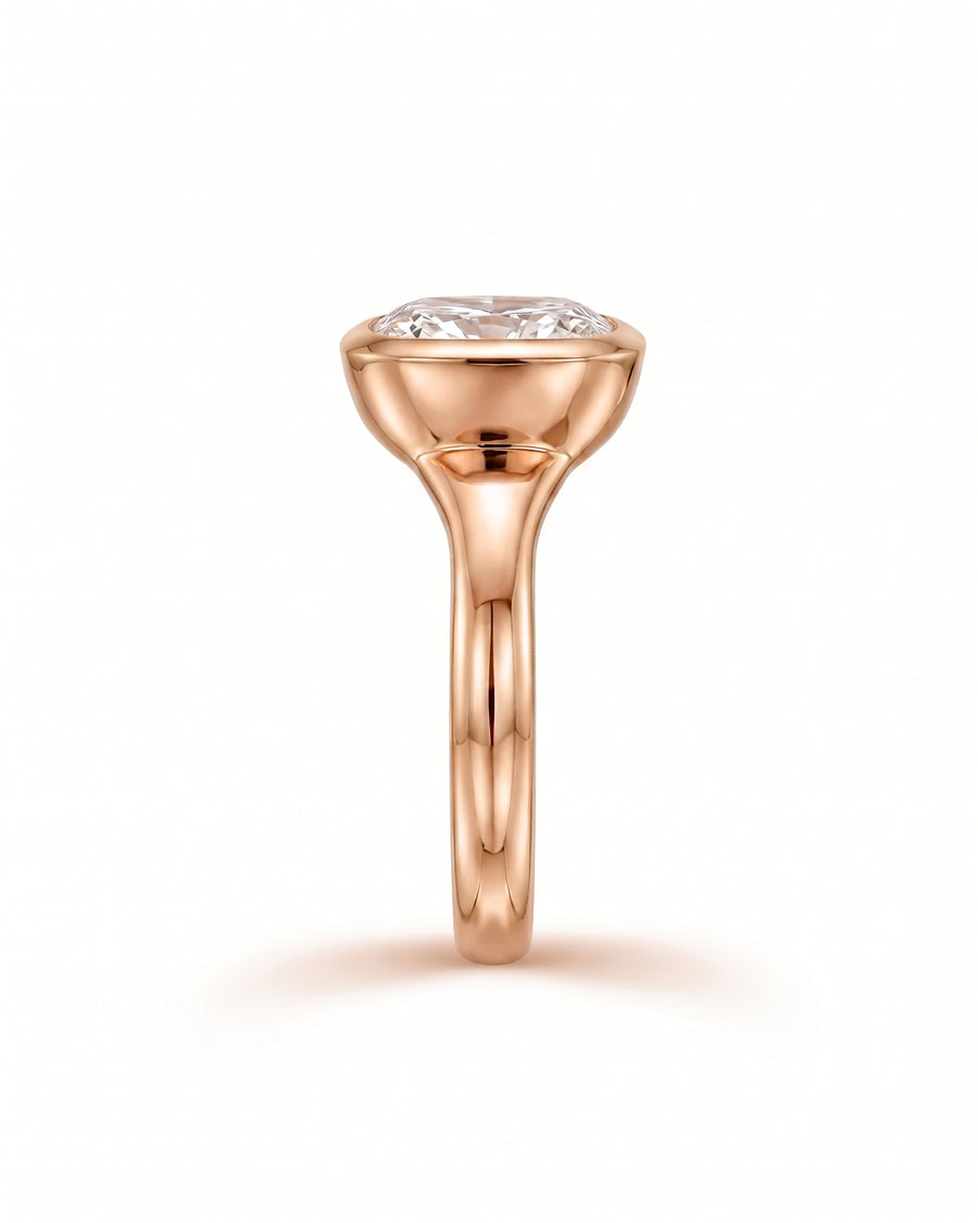 Rose gold engagement ring with a chunky cushion cut diamond in a bezel setting.