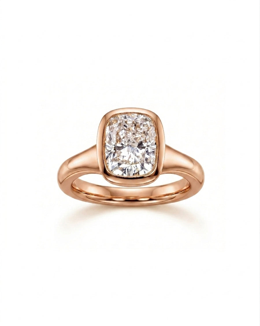 Rose gold engagement ring with a chunky cushion cut diamond in a bezel setting.