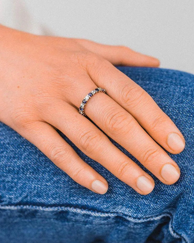 Claw set full eternity ring with alternating blue and clear gemstones on a hand.