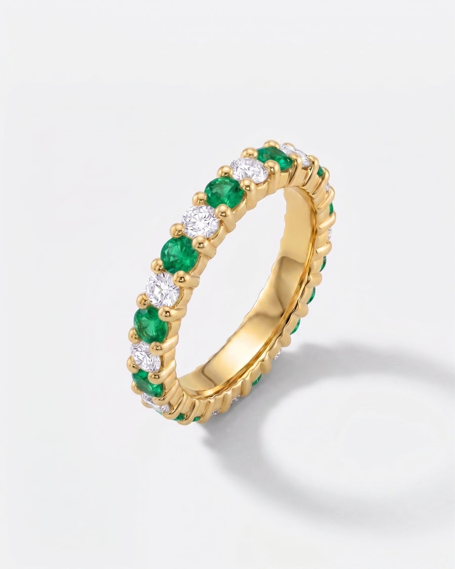 Gold full eternity ring with claw-set emeralds and diamonds.