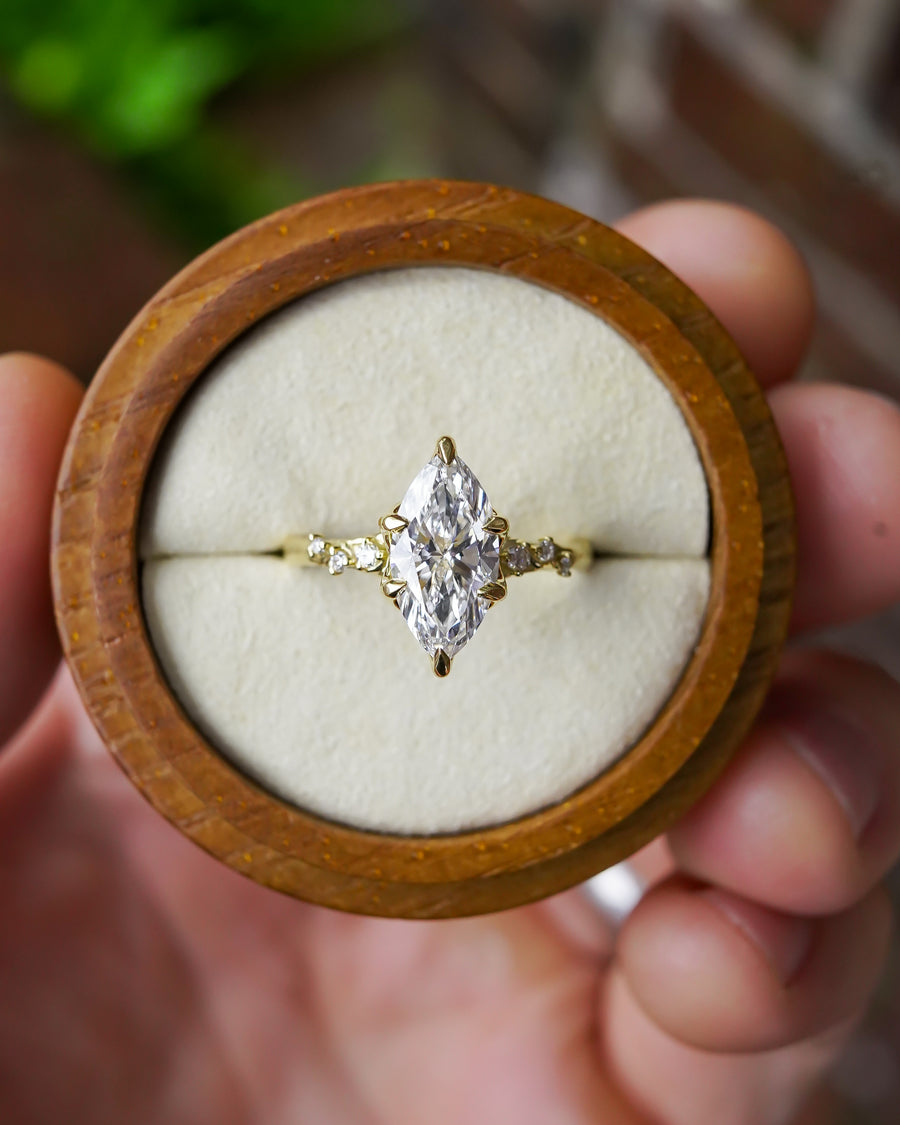 Marquise-cut lab-grown diamond engagement ring with a gold floral vine band in a wooden ring box.
