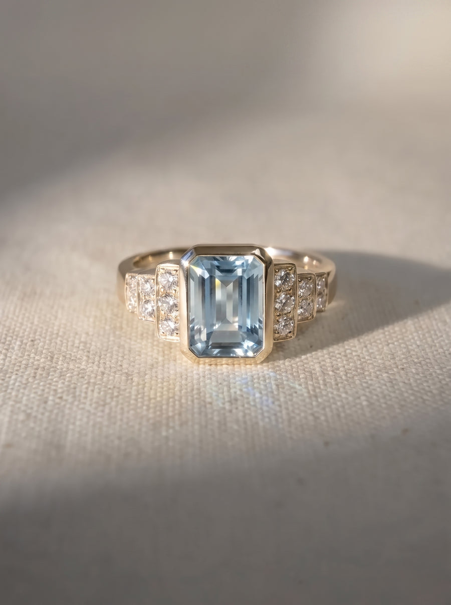 Art deco gold engagement ring with an emerald-cut aquamarine center stone and diamond side accents.