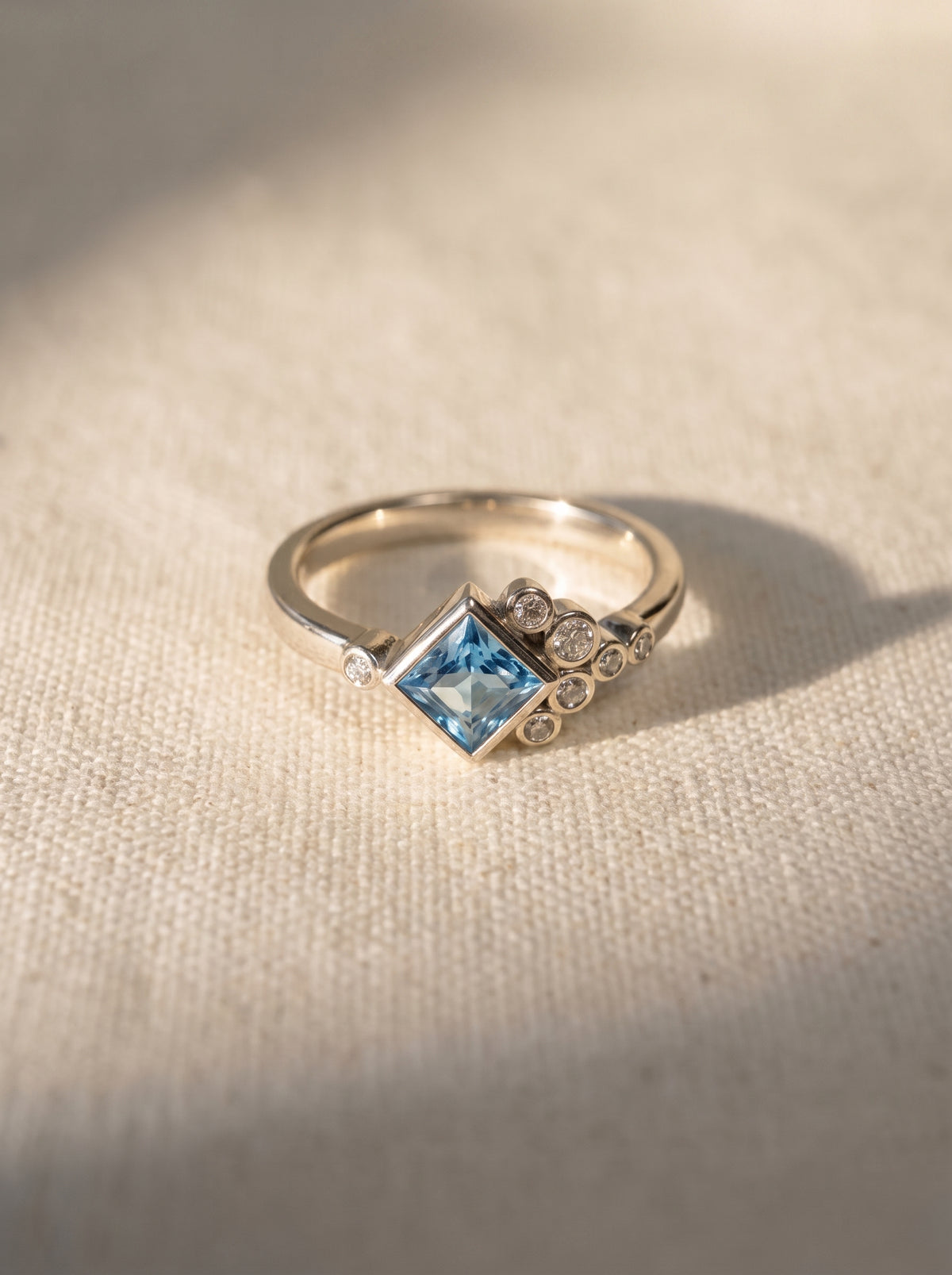 Silver engagement ring featuring a square blue gemstone accented by small round diamonds in a cluster design.