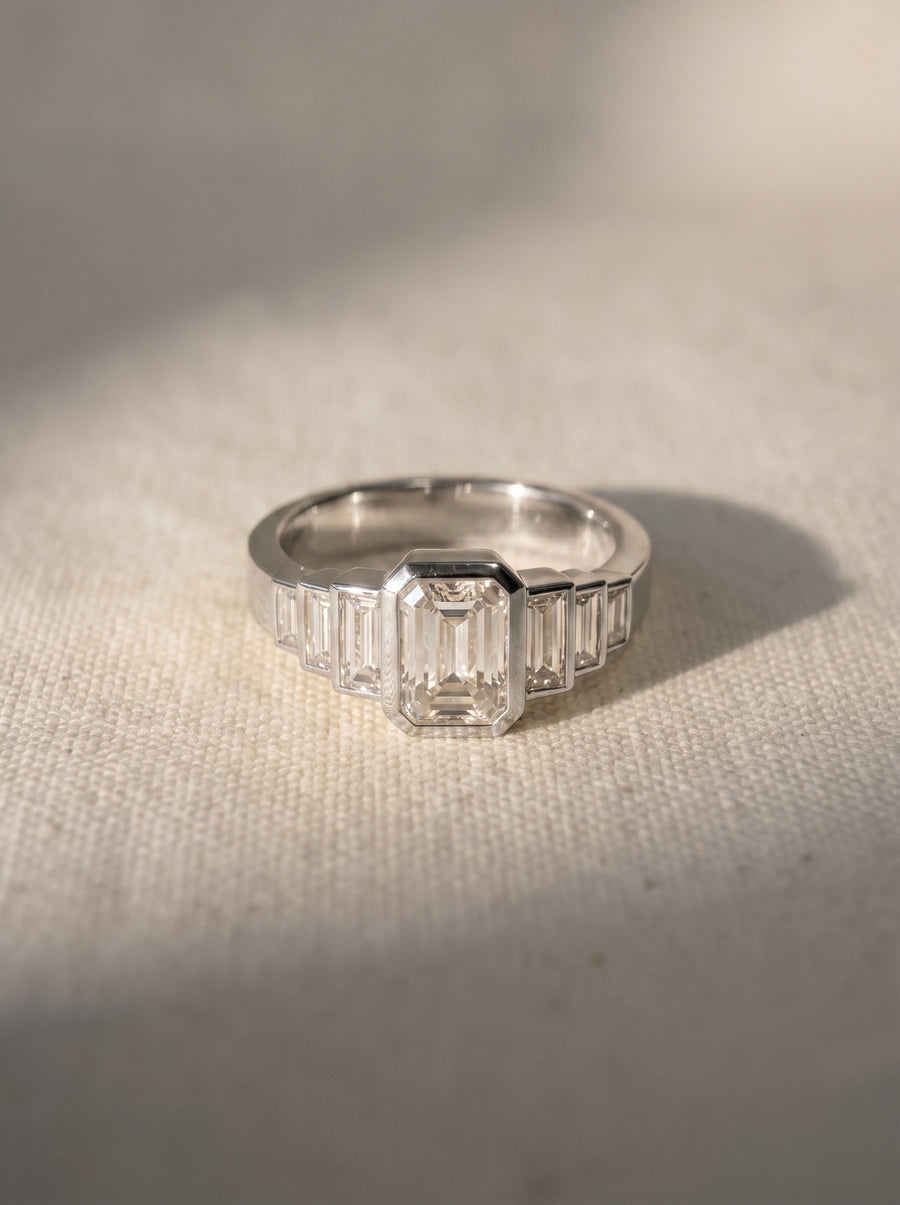 Platinum engagement ring with an emerald cut center diamond and baguette side stones in an art deco style.