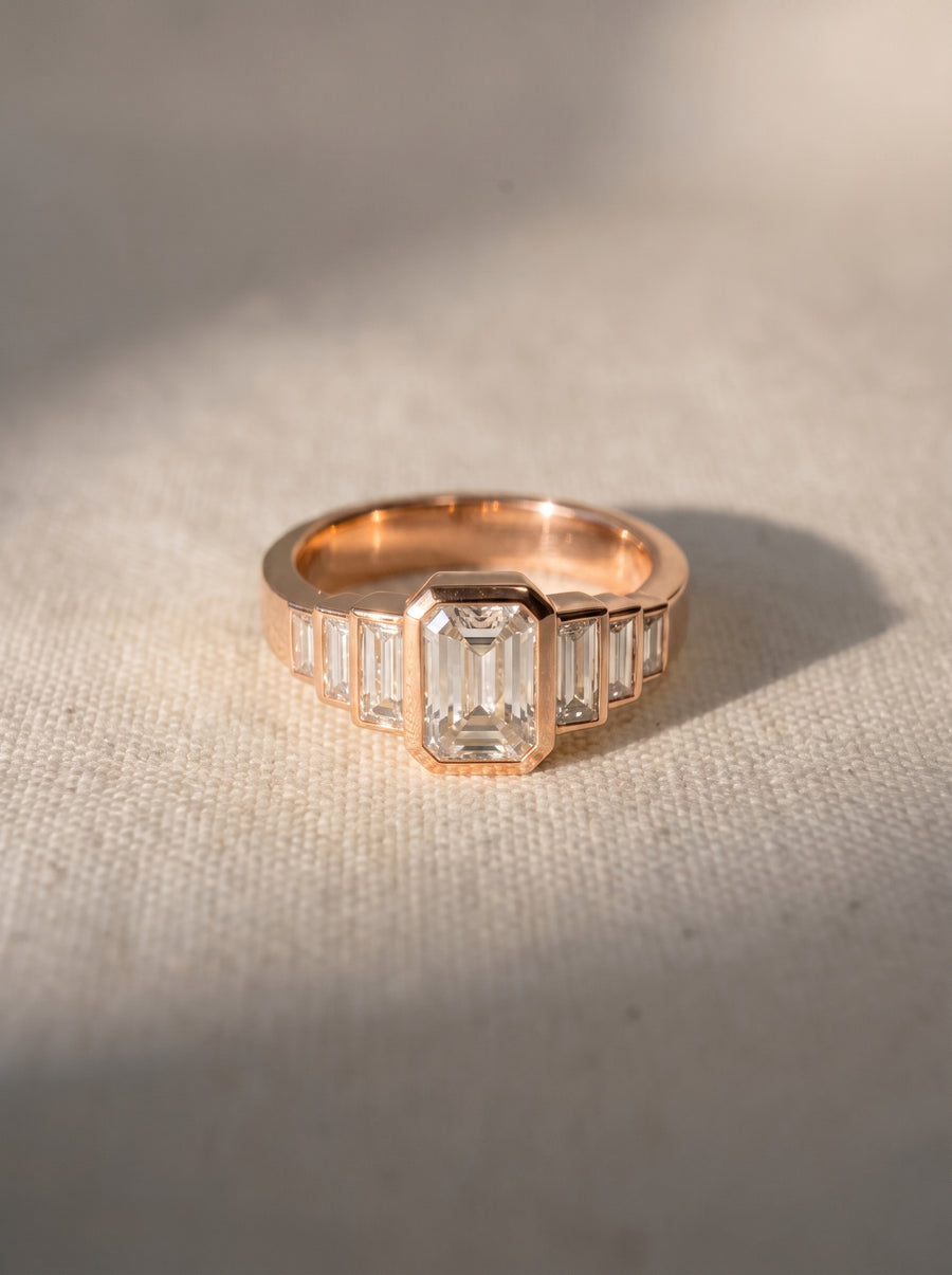 Rose gold engagement ring with a central emerald cut diamond and three baguette diamonds on each side.