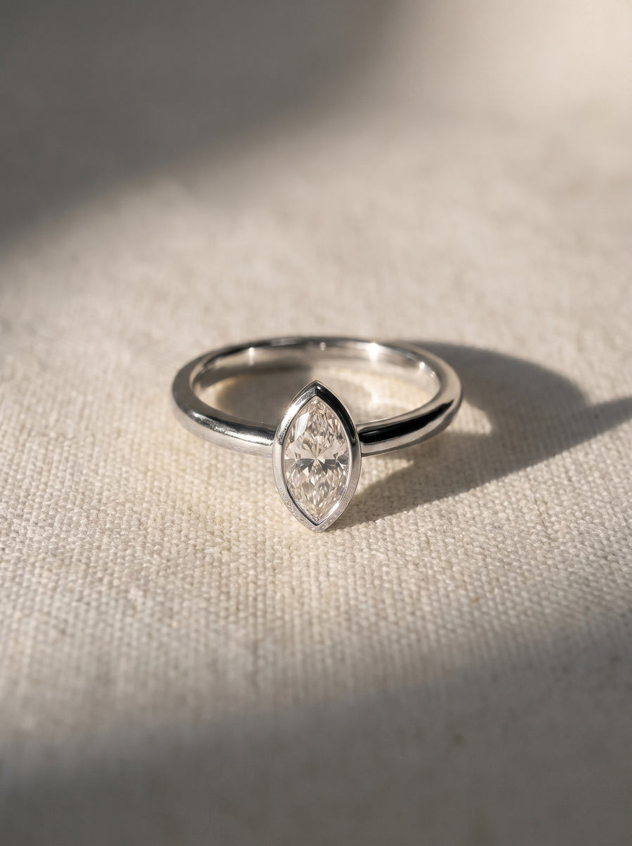 Marquise cut diamond engagement ring in a silver-toned bezel setting on a textured fabric background.