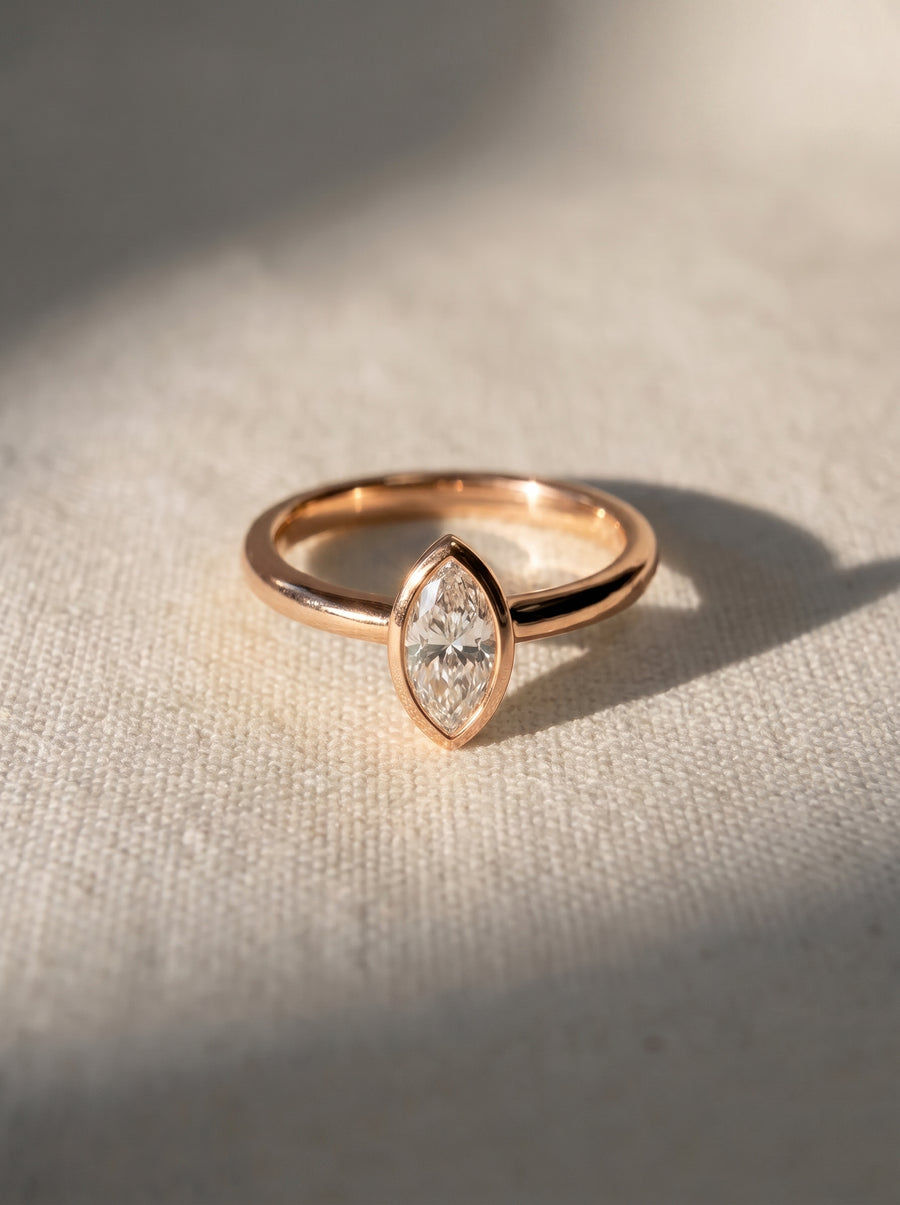 Marquise cut diamond engagement ring in a rose gold bezel setting on a textured fabric background.
