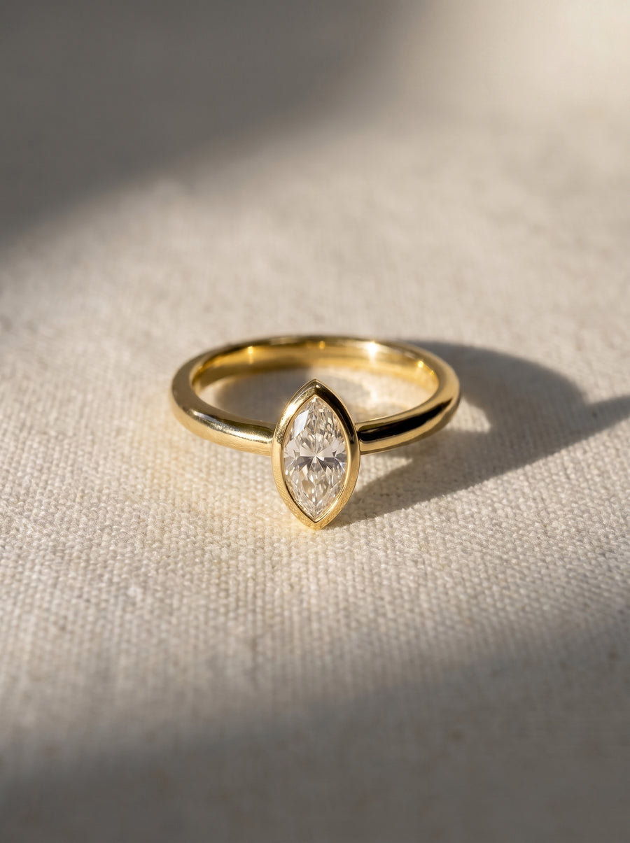 Marquise cut diamond engagement ring in a gold bezel setting on a textured fabric surface.