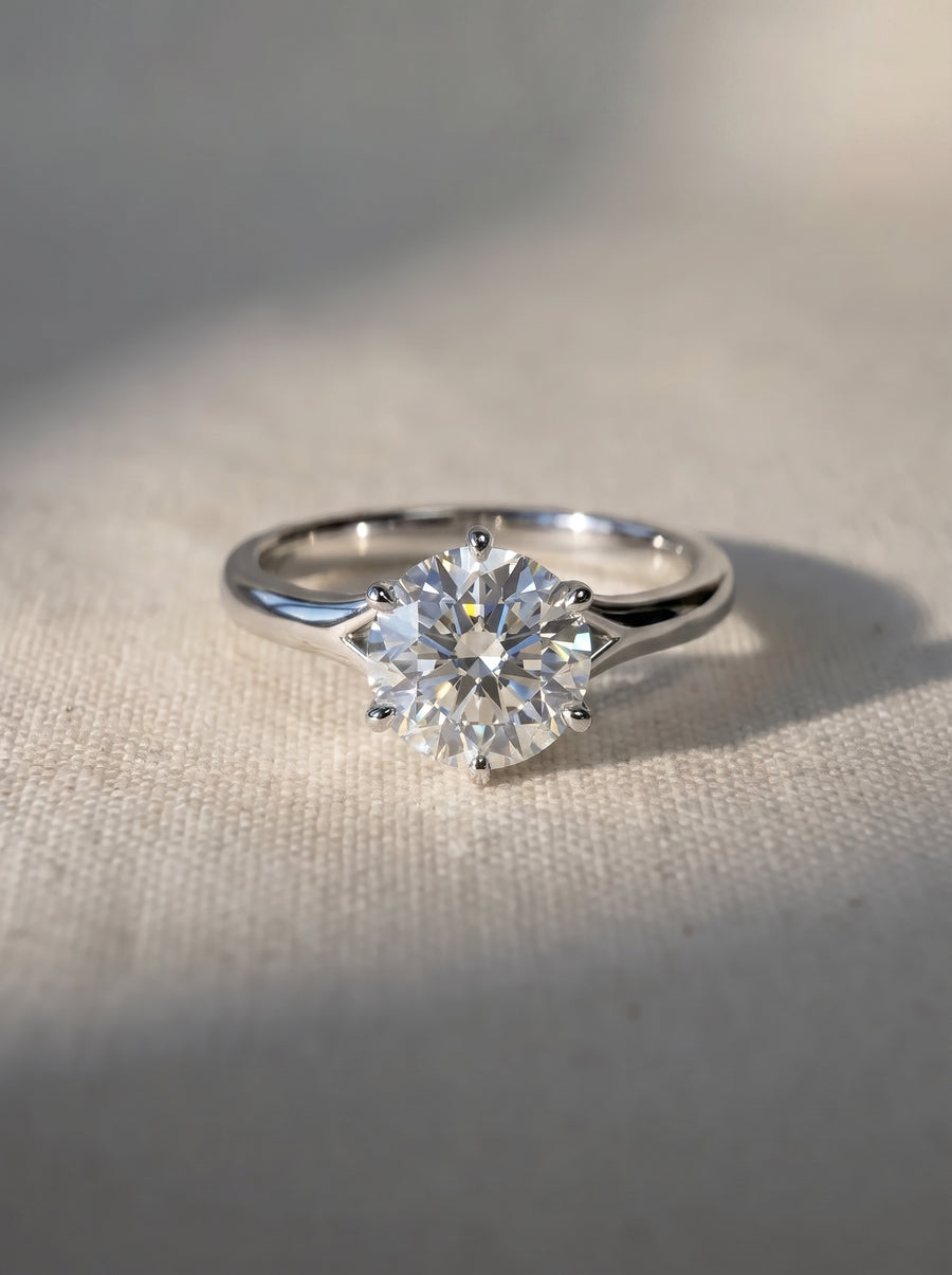 Round cut diamond engagement ring in a silver-toned metal band with a six-prong tulip claw setting.