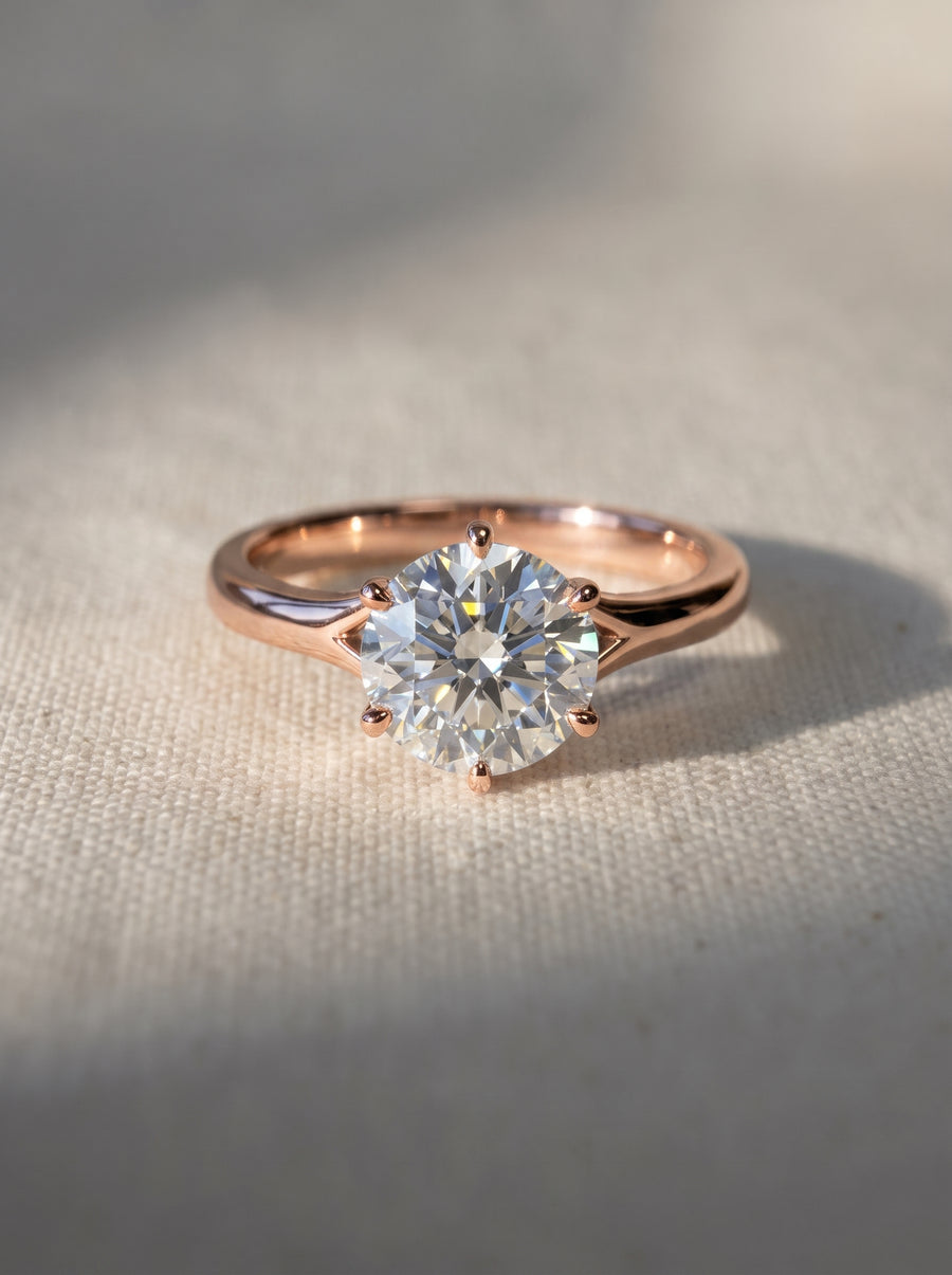 Round cut diamond engagement ring in a rose gold tulip claw setting on a textured fabric background.