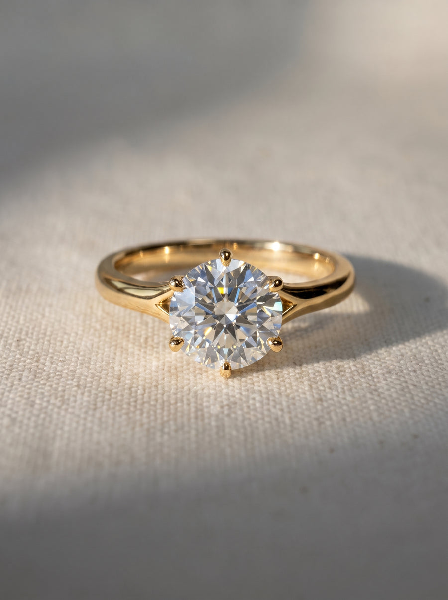 Round cut diamond engagement ring in a gold tulip claw setting on a textured fabric background.
