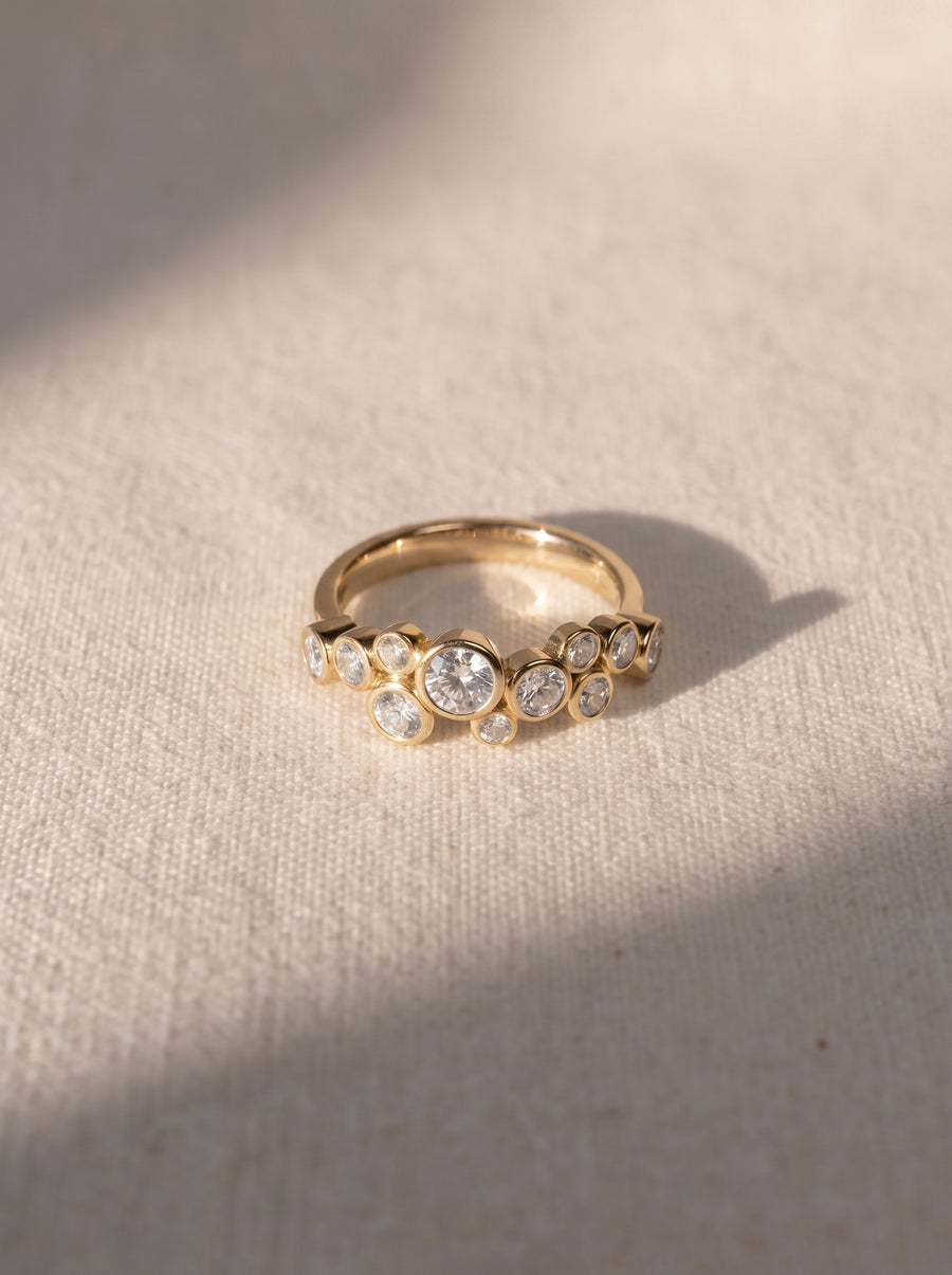 Gold ring featuring a cluster of round-cut bezel-set diamonds in a bubble design on a textured surface.
