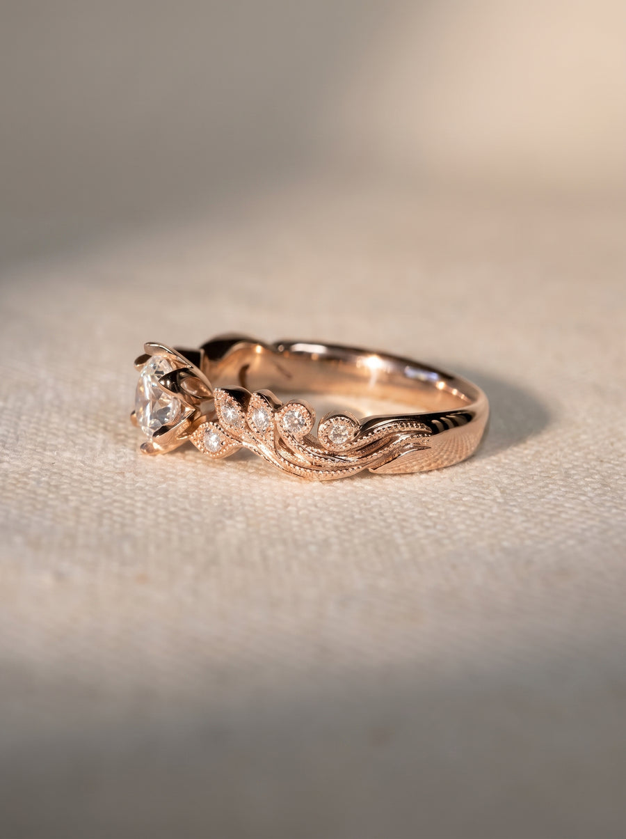 Rose gold engagement ring with a central diamond and beaded, leaf-inspired detailing on the band.