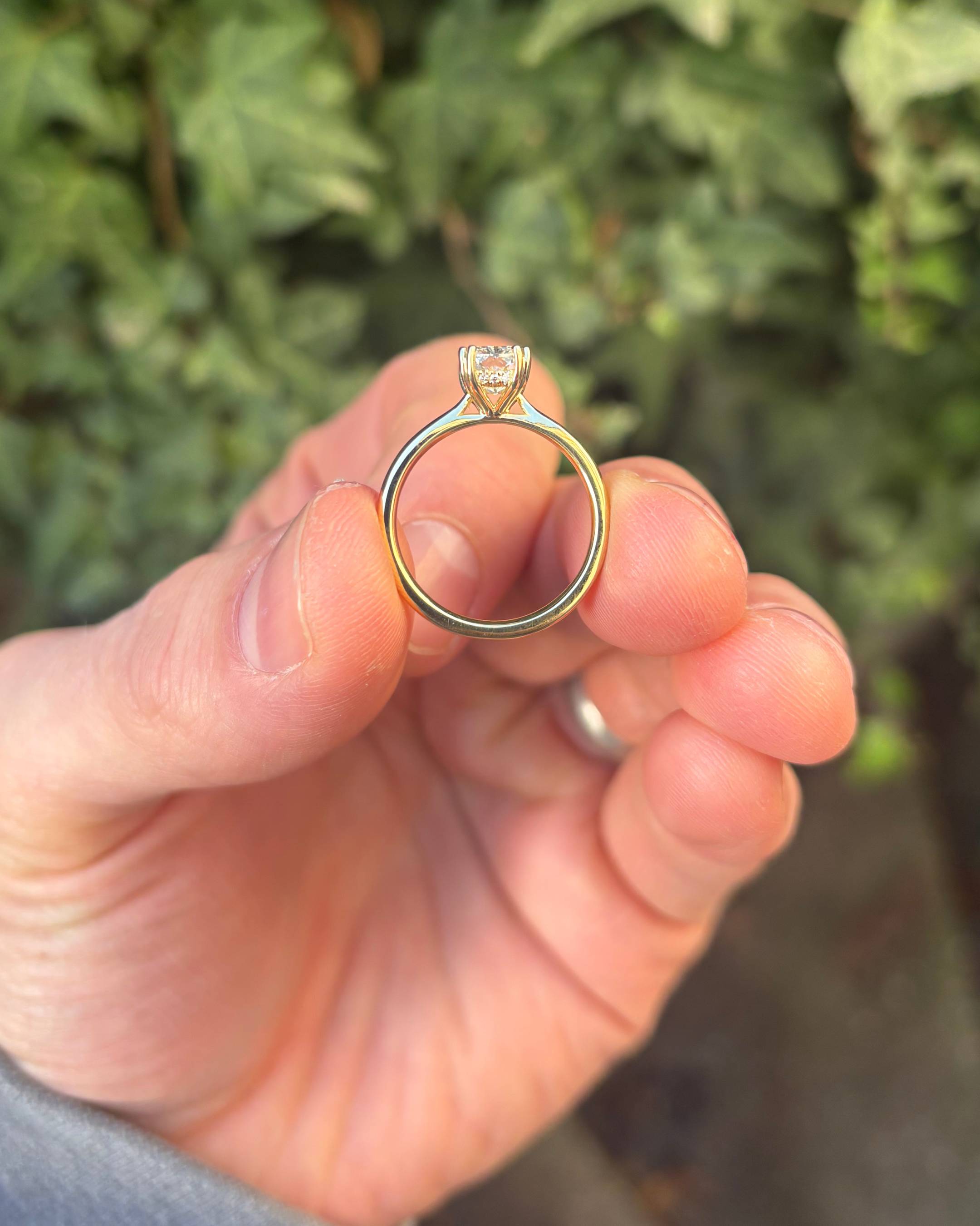 Gold ring with a diamond held between thumb and forefinger against a blurred green background