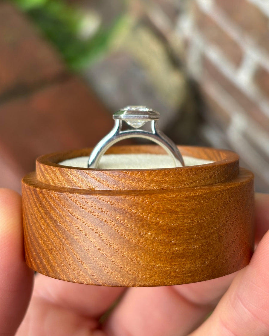 Emerald cut lab-grown diamond engagement ring in a silver bezel setting on a wooden ring box.