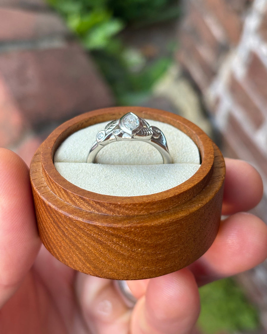 Silver marquise diamond engagement ring with leaf-inspired metal detailing in a round wooden box.
