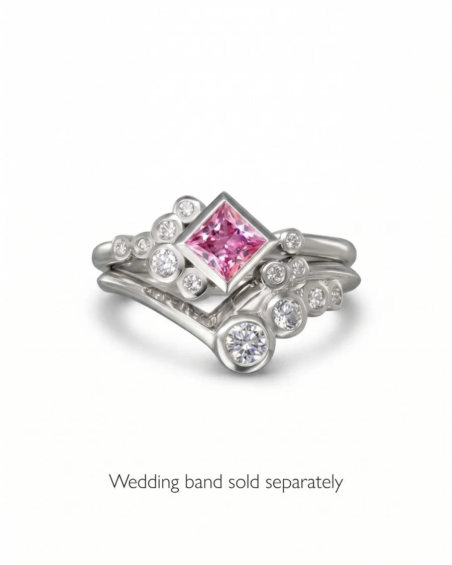 Platinum engagement ring featuring a princess-cut pink sapphire surrounded by bezel-set round white diamonds.
