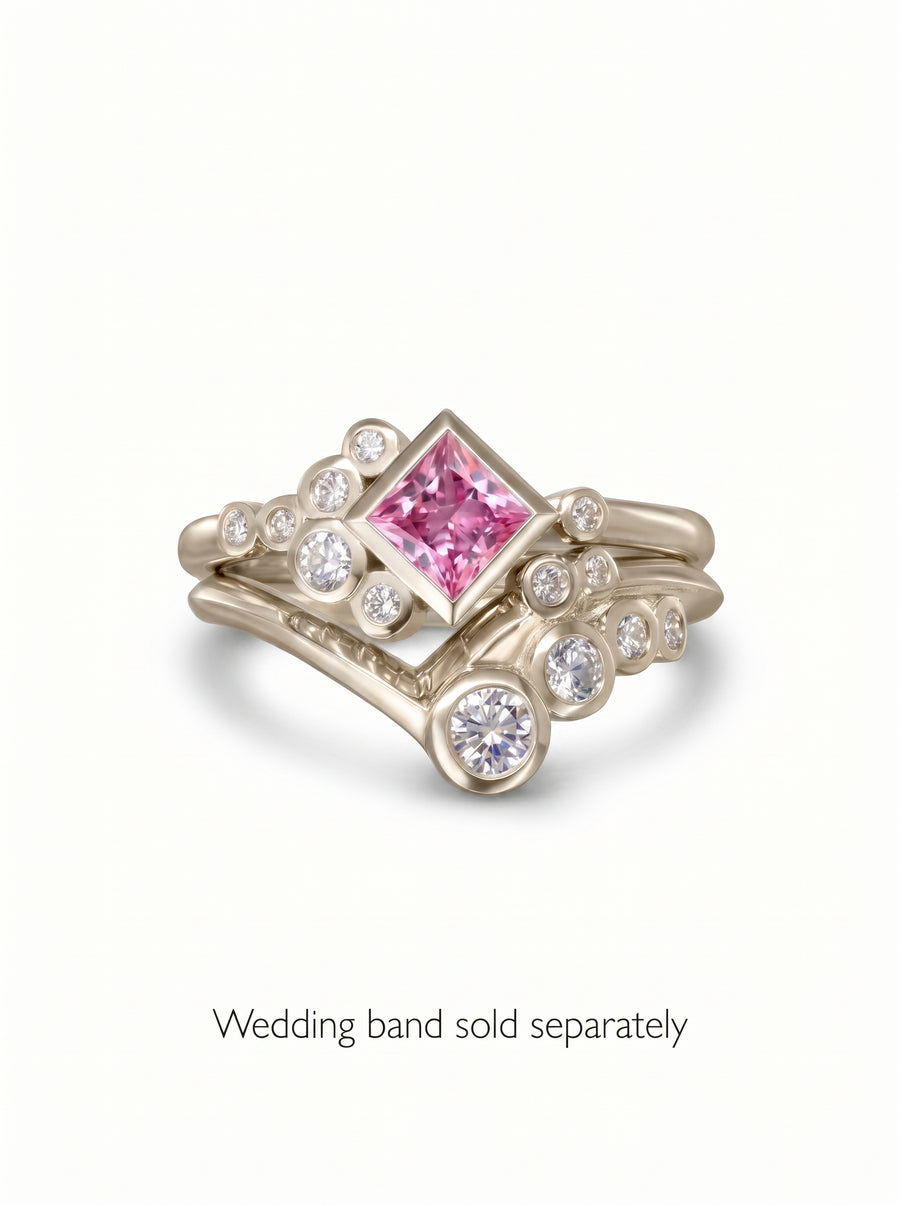 Gold engagement ring featuring a princess-cut pink gemstone surrounded by small round diamonds in a bubble design.
