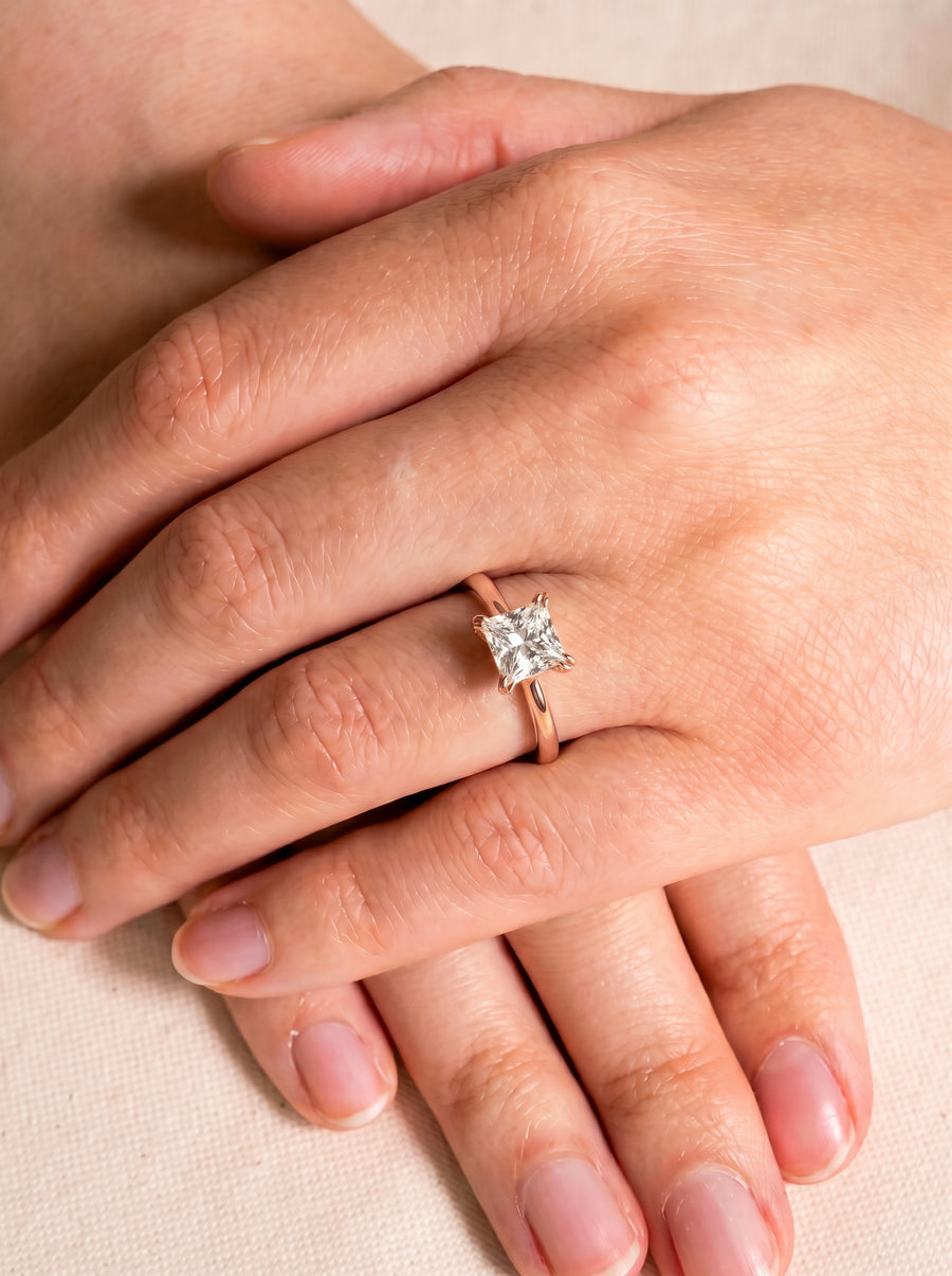 Princess cut diamond engagement ring with a hidden halo on a rose gold band worn on a finger.