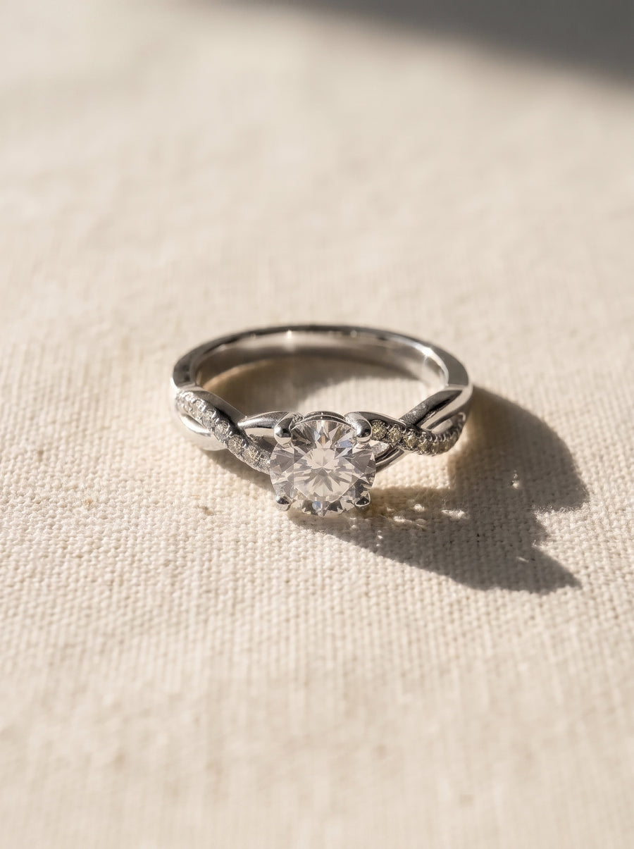 Round cut diamond engagement ring in a silver-toned metal with a twisted band and claw setting.