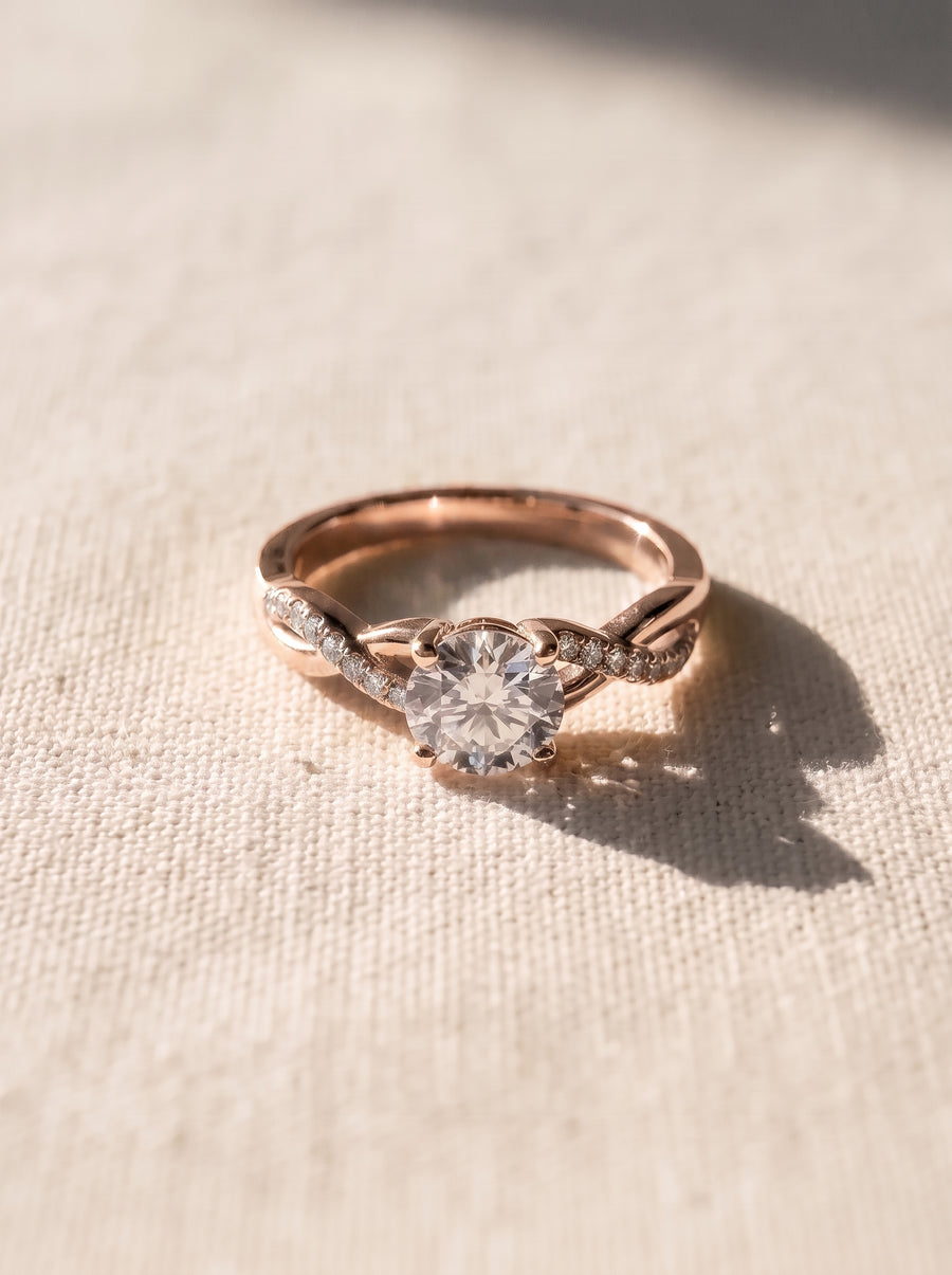 Rose gold engagement ring with a round cut center stone and a twisted band featuring small pavé diamonds.