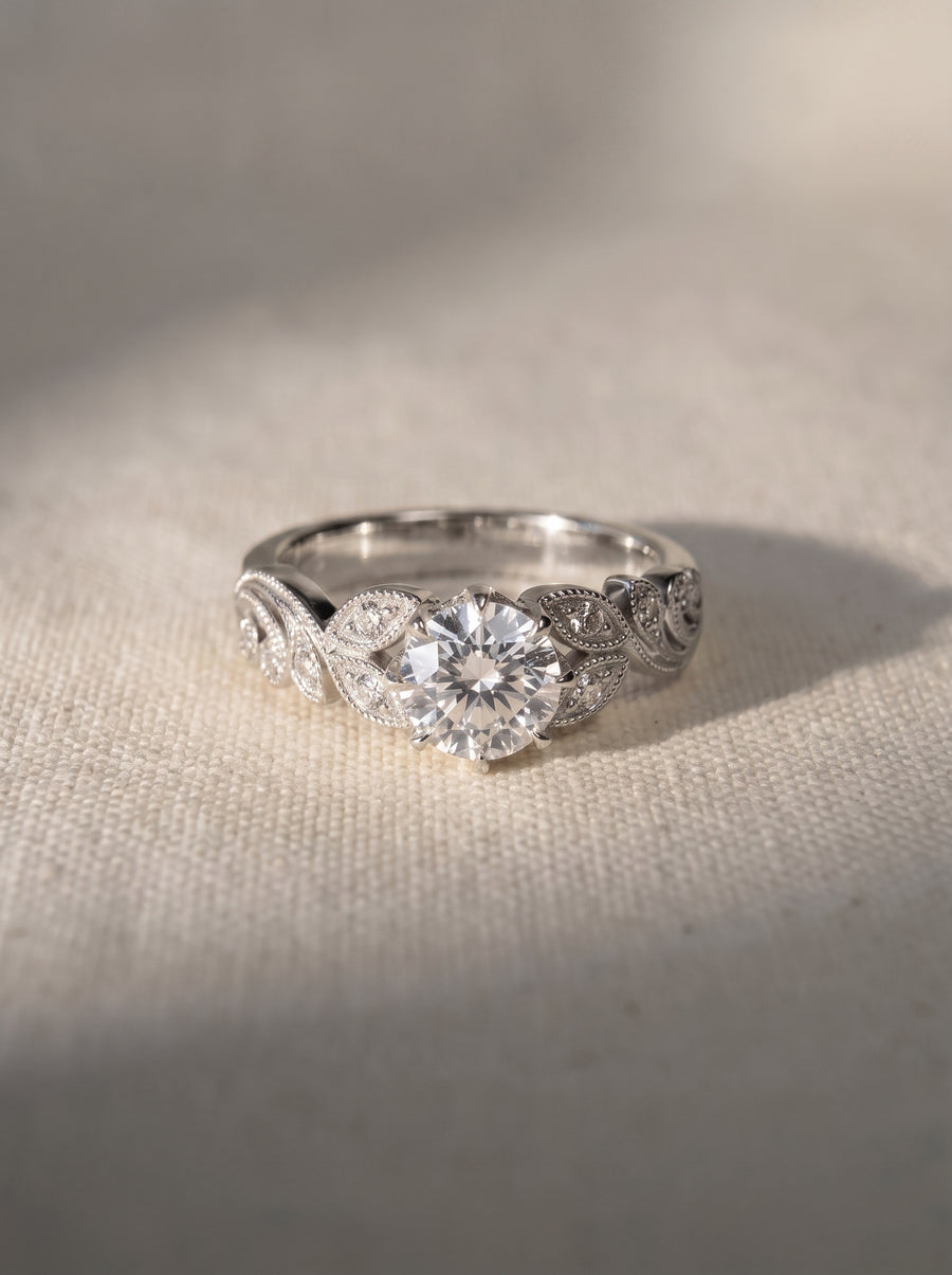 Platinum engagement ring featuring a round cut lab grown diamond with vintage leaf-inspired detailing on the band.