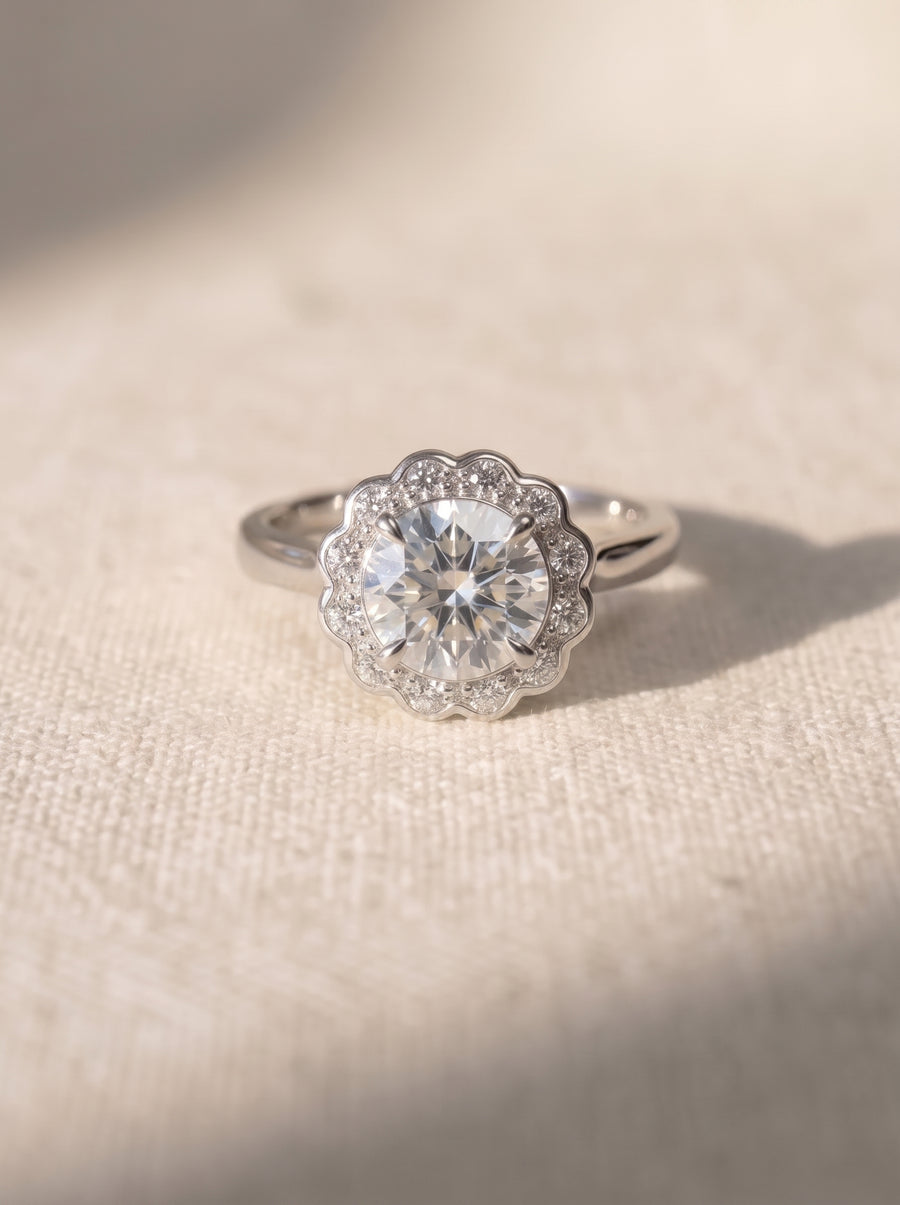 Silver engagement ring with a round diamond center stone in a scalloped halo setting on a textured surface.