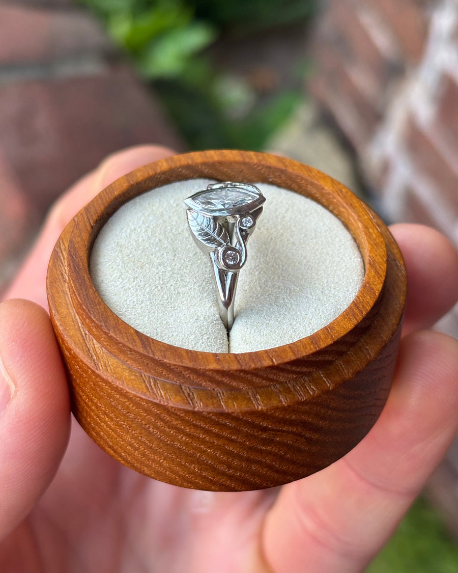 Marquise cut diamond engagement ring in silver with leaf-inspired metalwork in a wooden ring box.