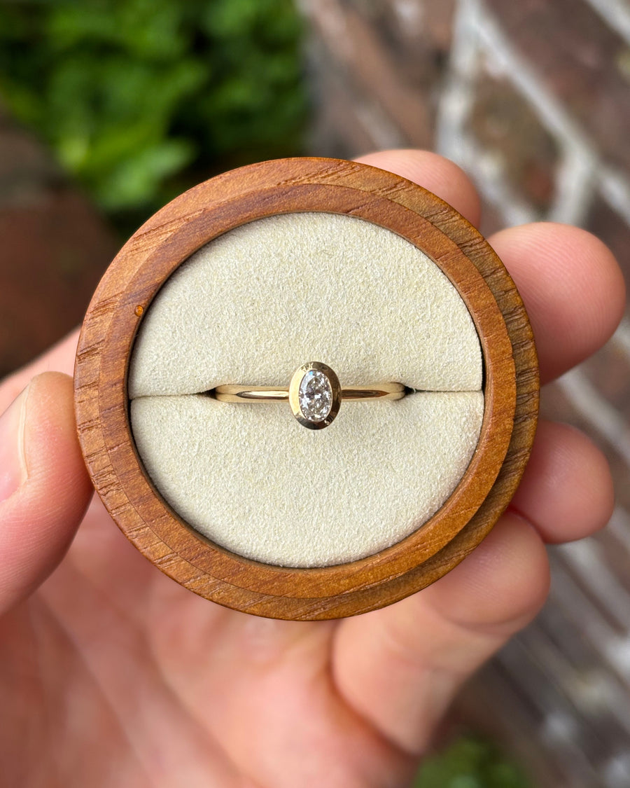 Oval cut diamond engagement ring in a 9ct yellow gold bezel setting held in a wooden ring box.