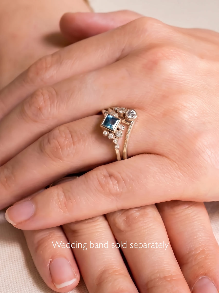 Gold engagement ring featuring a square blue gemstone and small round diamonds on a delicate band.