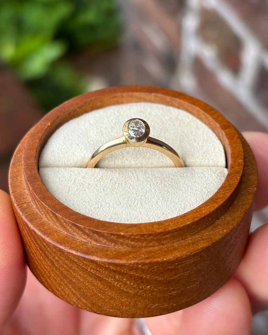 Oval cut diamond engagement ring with a gold bezel setting inside a wooden ring box.