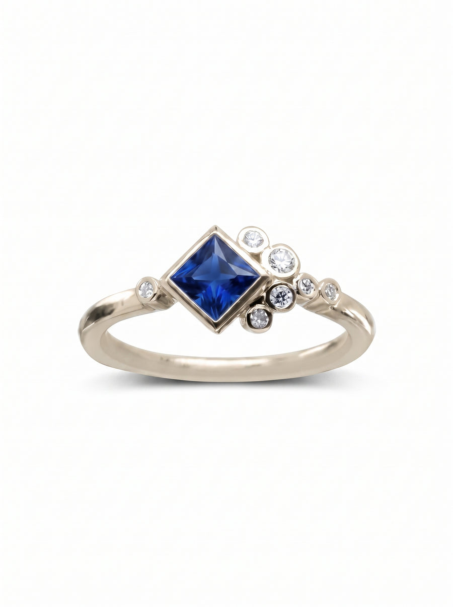 Gold engagement ring with a princess-cut blue sapphire and a cluster of small round diamonds.