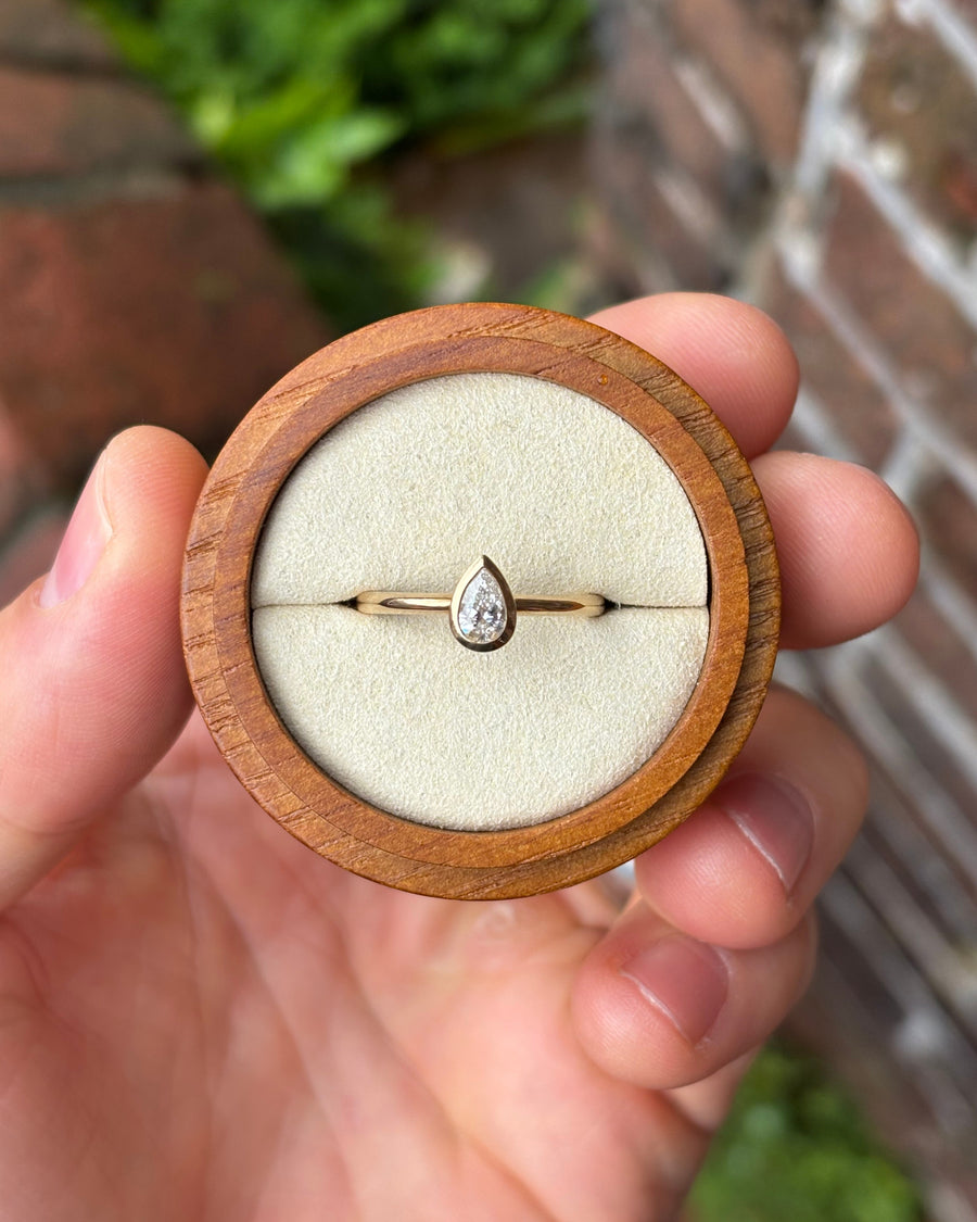 0.33ct pear cut diamond engagement ring in a 9ct yellow gold bezel setting held in a wooden box.