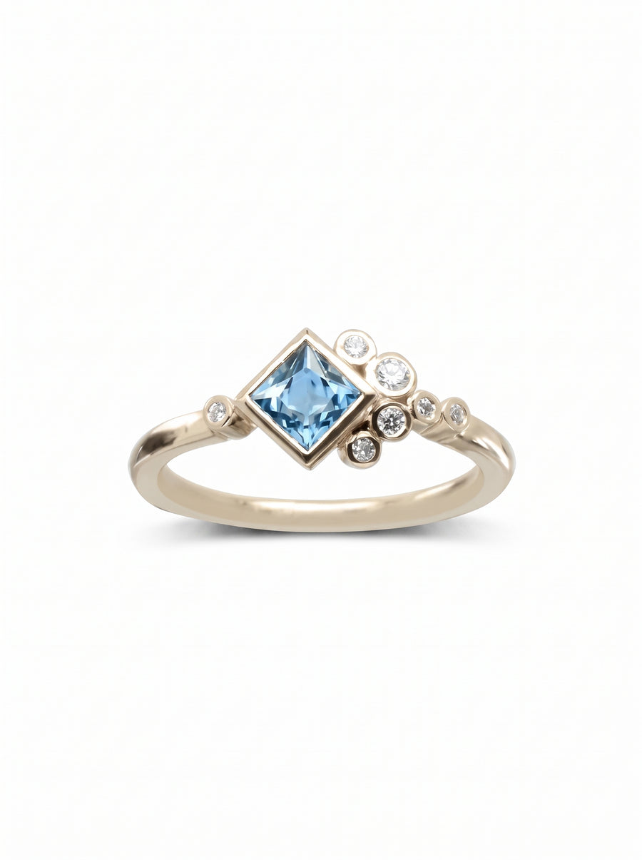 Gold engagement ring featuring a square blue gemstone accented by a cluster of round white diamonds.