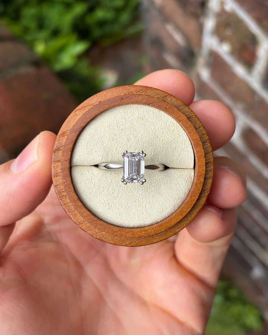 Emerald cut lab-grown diamond engagement ring with a hidden halo in a platinum setting inside a wooden box.