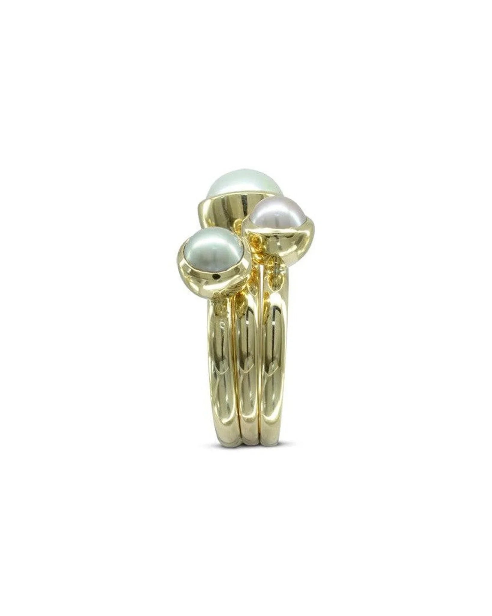 Stacked gold rings set with three round pearls, modern organic design, jewelry on white background.