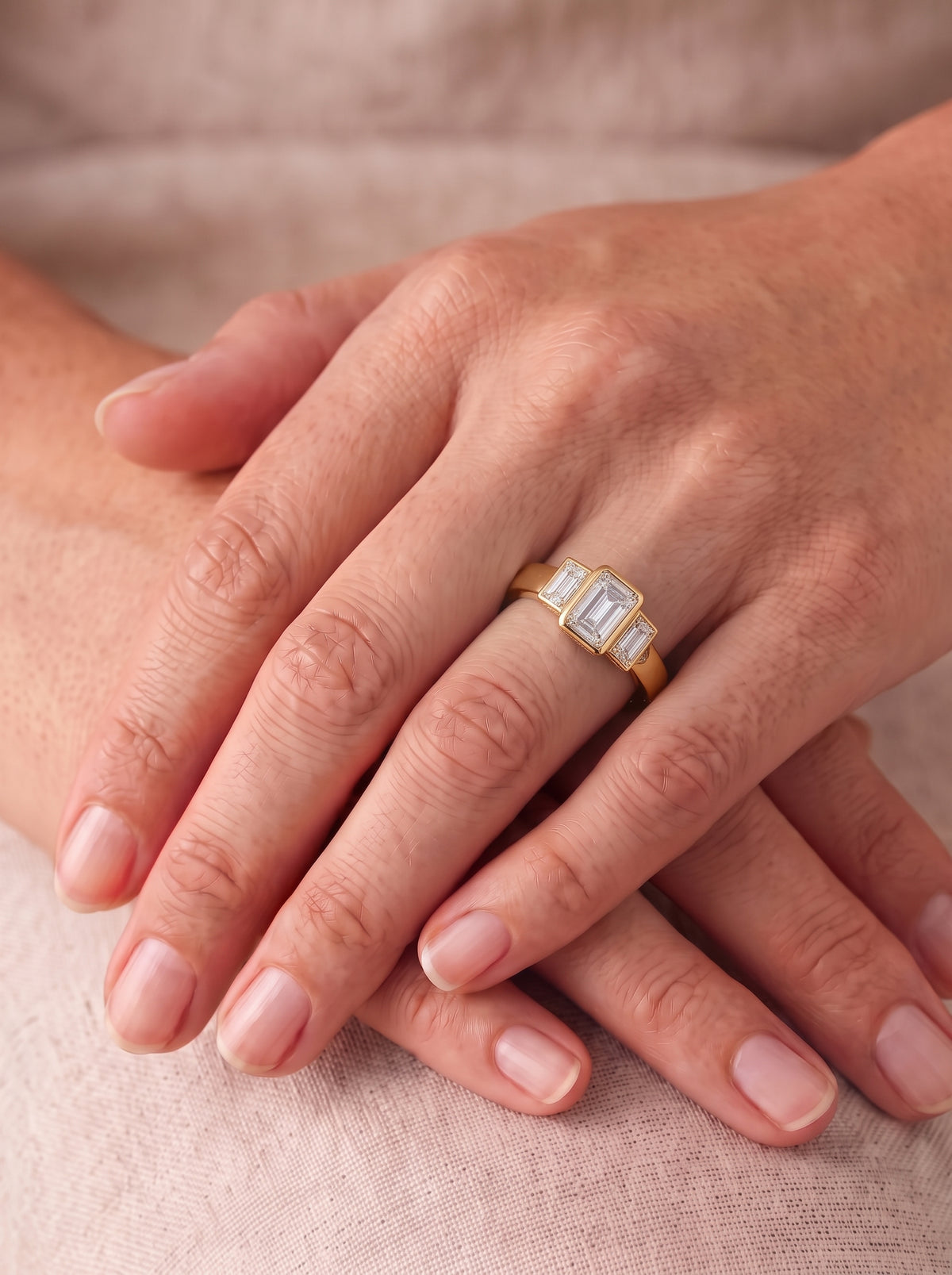 Gold trilogy ring featuring a central emerald-cut diamond flanked by two baguette-cut diamonds on a smooth band.
