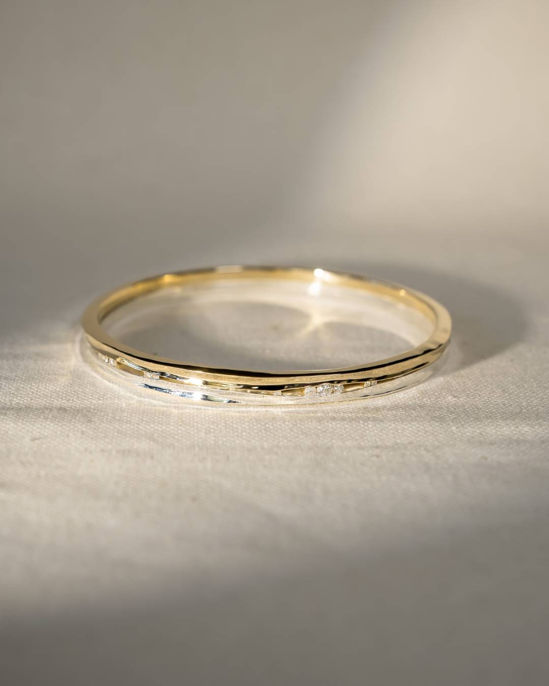 Elegant gold and silver bangle with hammered texture and small diamonds on linen fabric