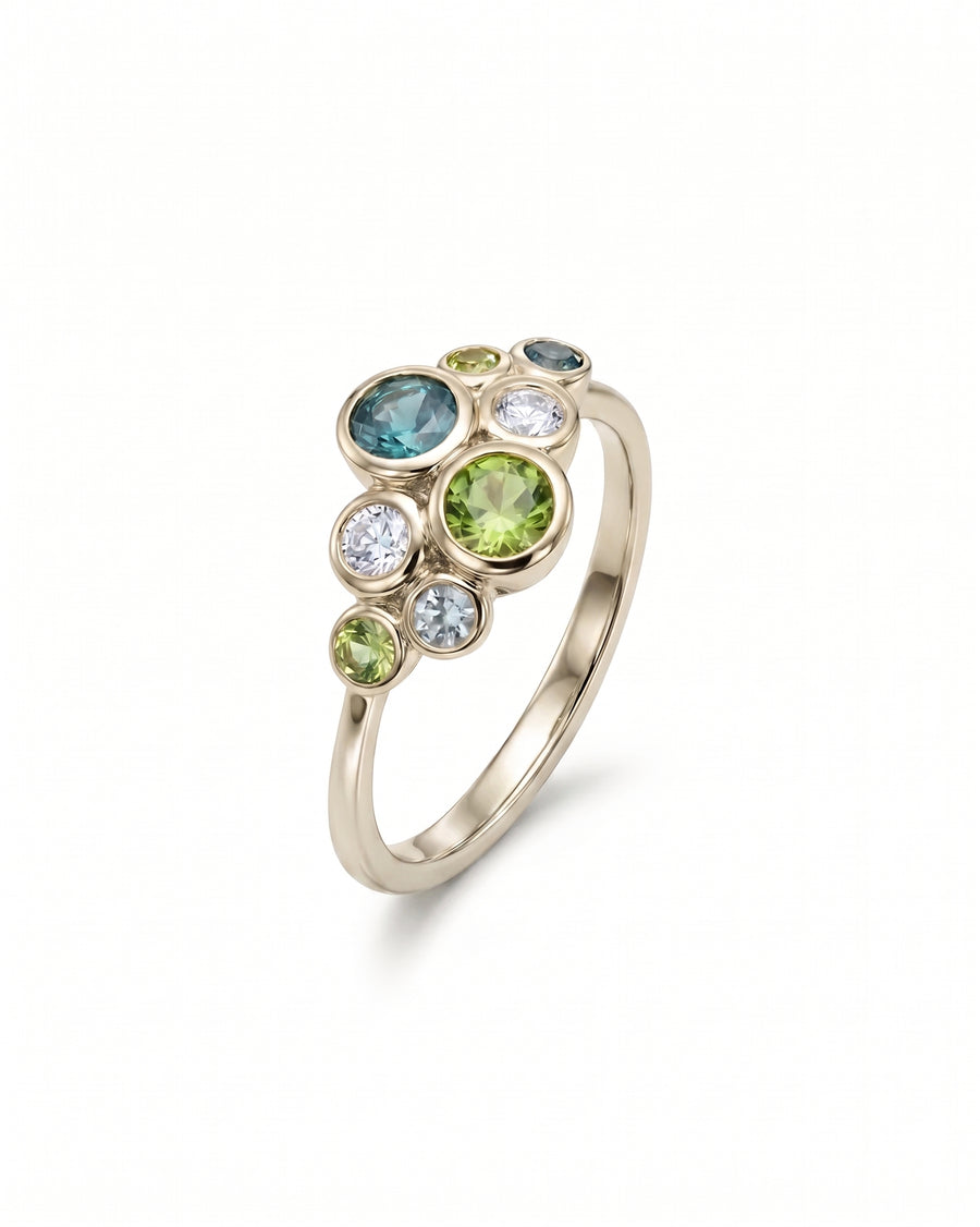 Gold cluster ring featuring bezel-set green and teal sapphires and clear round stones.