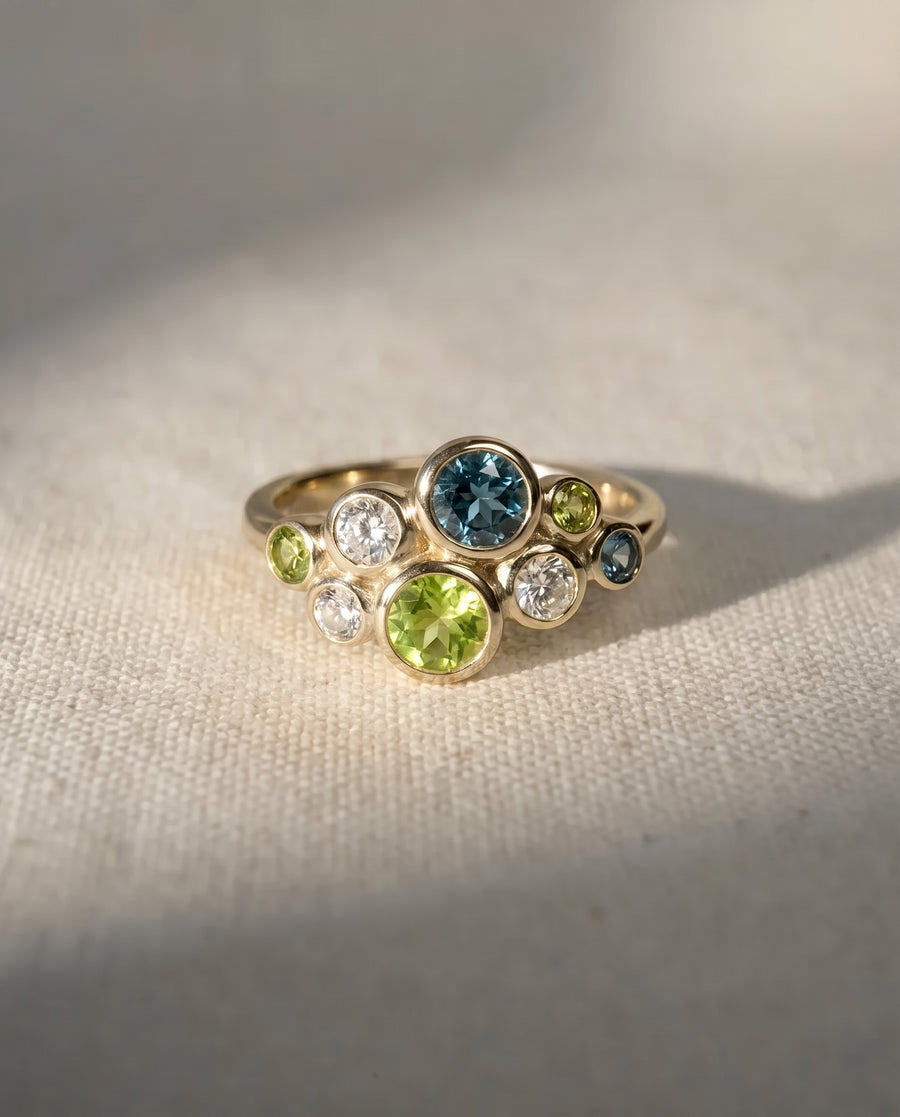 Gold cluster ring featuring bezel-set green and teal sapphires and clear diamonds in a bubble design.