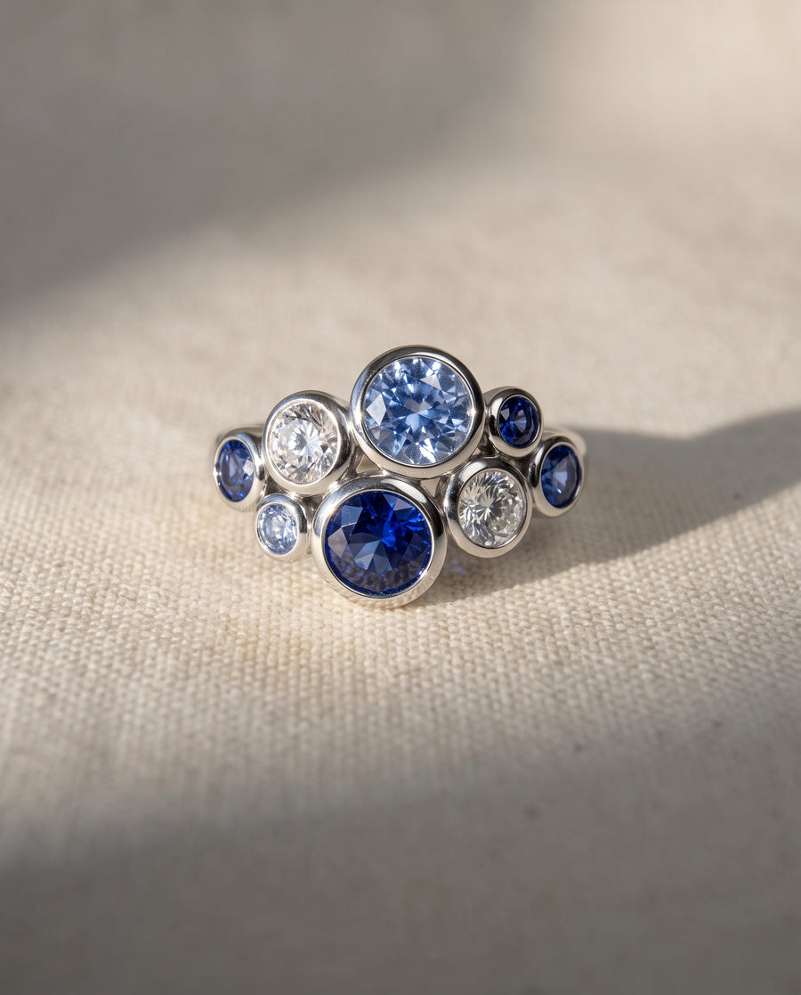Platinum cluster ring featuring bezel-set blue sapphires and round diamonds in a bubble-inspired arrangement.